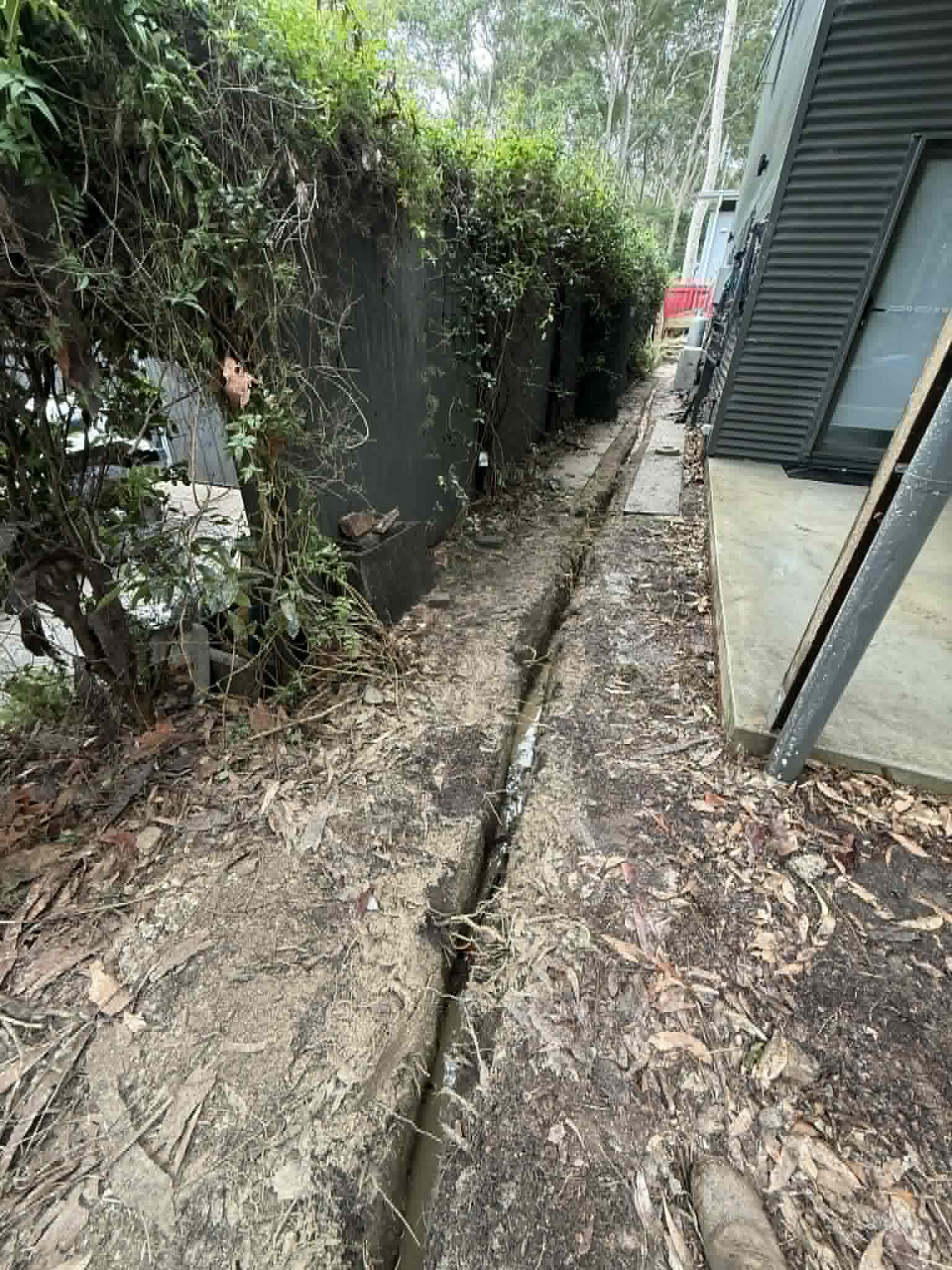 A GreenVac trench running along a narrow passage between a house and established planting